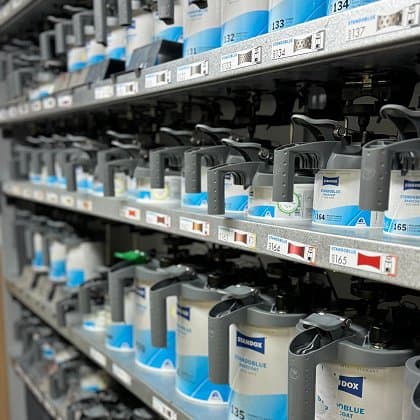 Regale mit verschiedenen Autolackfarben und Sprühdosen in einer Lackierwerkstatt, geordnet nach Farbcodes, bereit für den Einsatz bei Smart Repair.